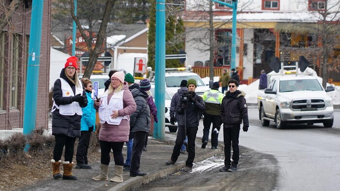 Des gens et des médias attendent sur un trottoir au centre-ville d'Amqui.