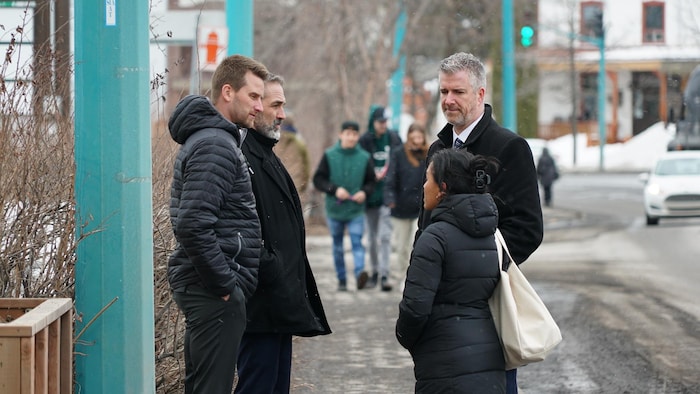 Quatre personnes discutent sur un trottoir. 