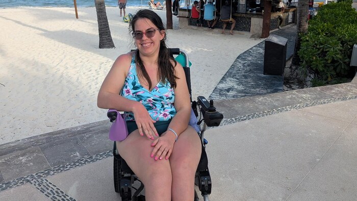Amy Adair est assise dans un fauteuil roulant et porte un chandail fleuri.