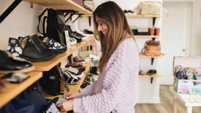 Ana María Arroyave touche un accessoire posé sur une étagère garnie de souliers et de sacs dans sa boutique.