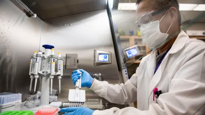 Une homme avec un sarrau manipule des instruments de laboratoire. 