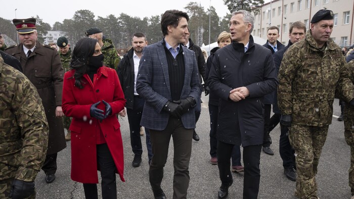 Anita Anand marche avec le premier ministre Justin Trudeau et Jens Stoltenberg lors de leur visite d'une base militaire.