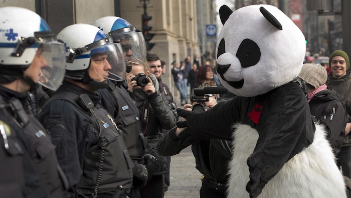 Un manifestant vêtu d'un costume de panda se tient devant une rangée de policiers.