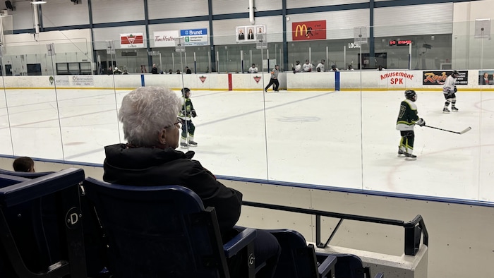 Une femme âgée regarde un match de hockey depuis les estrades.