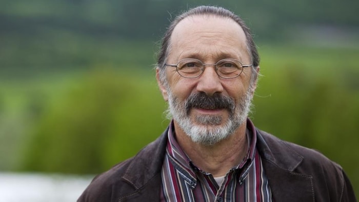 Portrait d’André Bélisle; à l'arrière-plan, de la verdure.