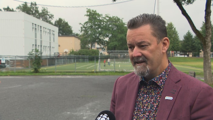 Un homme se tient près d'une école où des locaux modulaires ont été ajoutés.