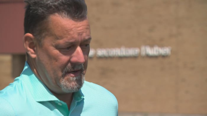 André Bernier devant la façade en briques de l'école secondaire de l'Aubier, à Lévis.