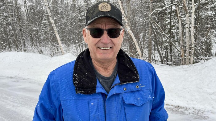 André Bouliane, souriant, portant des lunettes fumées et une casquette. Il est dans un paysage hivernal.