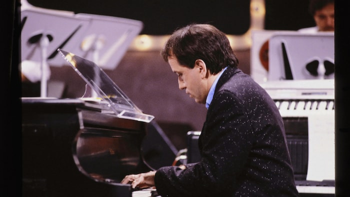 André Gagnon interprète une pièce sur un piano à queue.