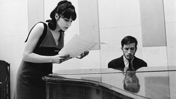 André Gagnon est assis au piano tandis que Renée Claude examine une partition.