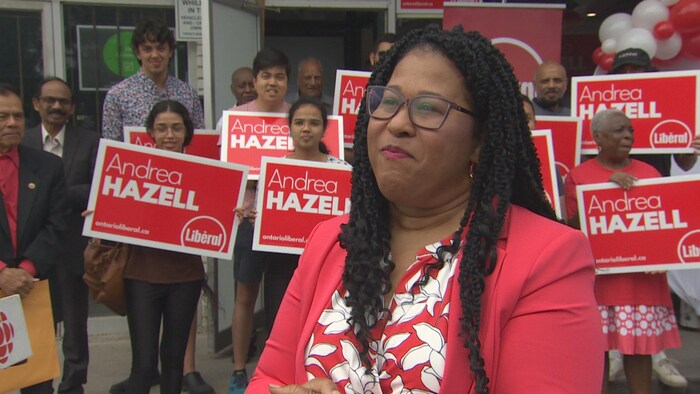 Andrea Hazell en entrevue devant une foule de partisans tenant des pancartes sur lesquelles son nom est inscrit.