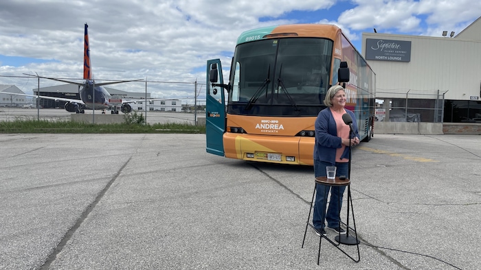 Andrea Horwath fait un point de presse sur le tarmac d'un aéroport, devant son autobus de campagne.