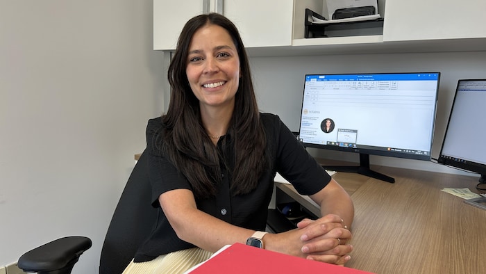 Une femme assise à son bureau regarde la caméra en souriant