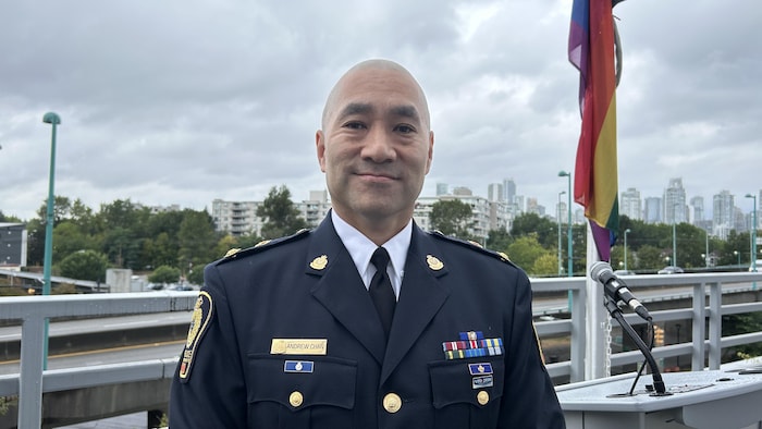 Andrew Chan sourit à la caméra. Il est à l'extérieur. Derrière lui, un drapeau de la fierté
