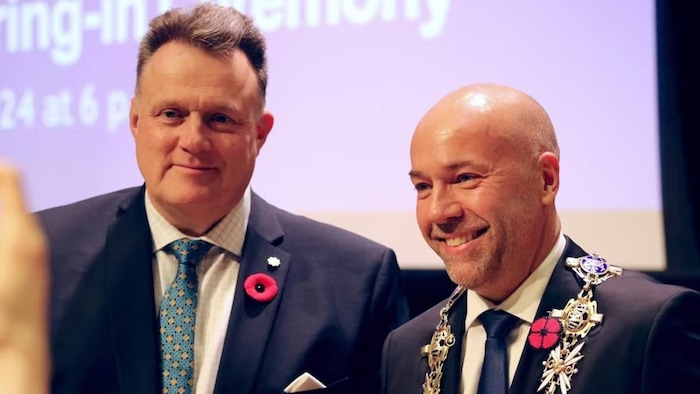 Deux hommes sourient pour la photo. Le nouveau maire porte la grande chaîne en or.