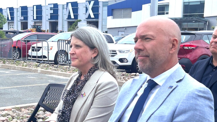 Deux personnes assises sur des chaises dans un stationnement, avec en arrière-plan un entrepôt décoré des lettres formant le mot Halifax.