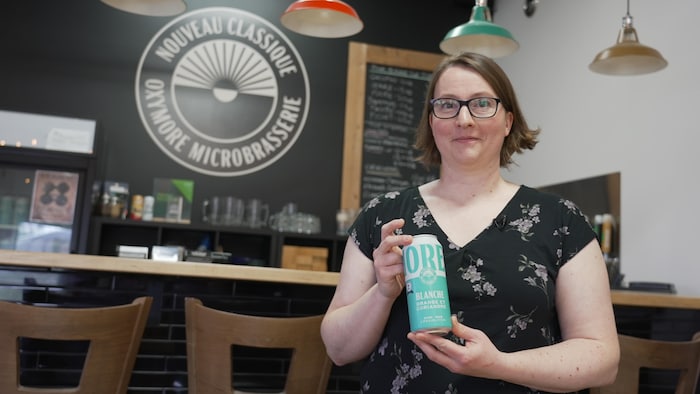Une femme habillée en noir tient une canette de bière de couleur turquoise dans une salle à manger.