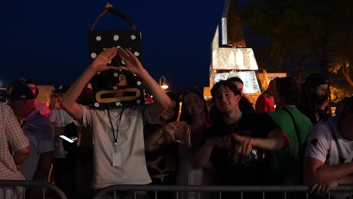 Une personne ayant les mains en triangle, munie d'une tête carrée noire à pois blancs.