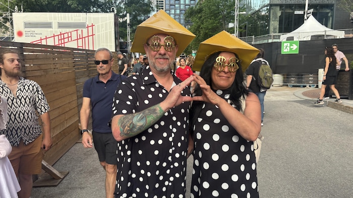 Deux personnes vêtus de vêtements à poids et de chapeaux triangulaires forment un triangle avec leurs doigts.