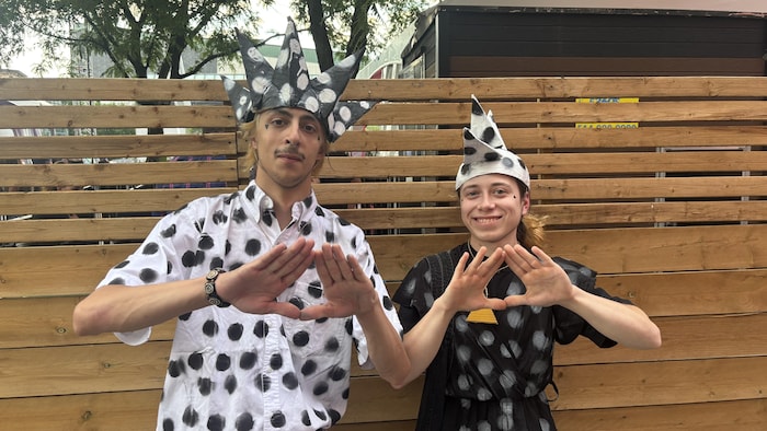 Deux personnes habillés de pois forment chacun un triangle avec leurs mains. 