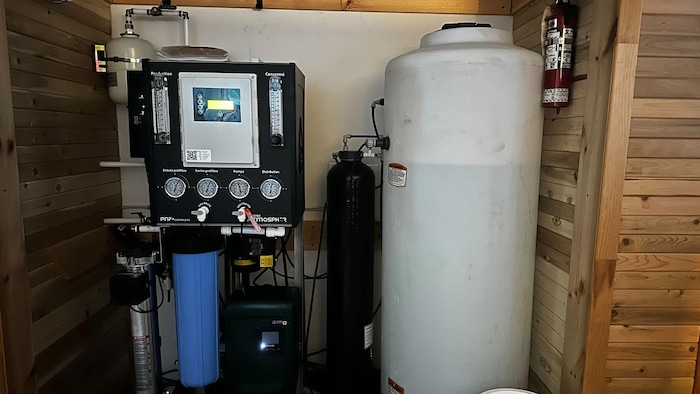 Un grand réservoir d'eau est installé avec plusieurs appareils de filtration dans le coin d'une pièce.