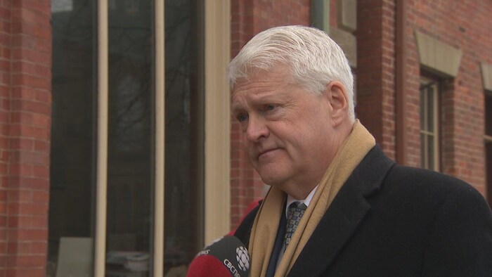 Angus Orford à l'extérieur devant un bâtiment, un micro de Radio-Canada pointé vers lui.