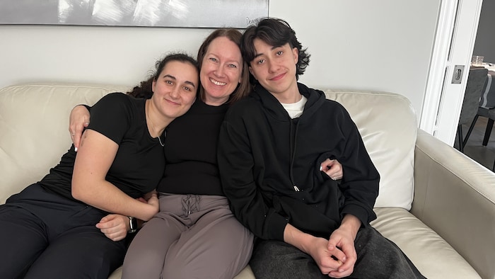 Une femme, sa fille et lad   fils sont assis dans un sofa. 