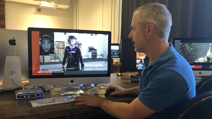 Jaky Fortin assis devant un écran d'ordinateur où on voit un personnage 3D.