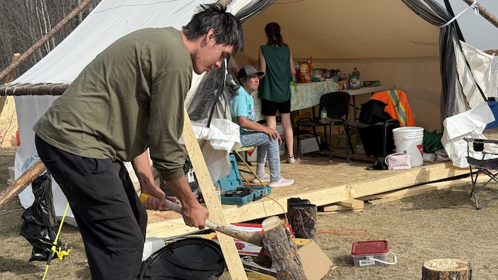 Keenan Nottawa fend une bûche avec une hache.