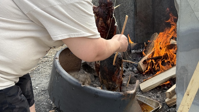 Une personne vérifie une outarde qui cuit sur le feu dehors.