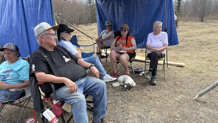 Des Abitibiwinniks profitent d'un moment autour d'un feu de camp près de tentes et d'une forêt.