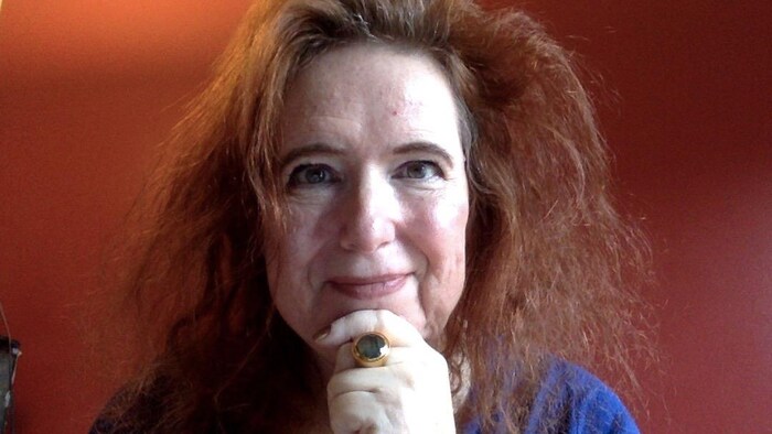 Une femme fixe l'appareil-photo en se tenant le menton.