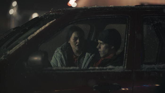 Une femme et un homme dans une voiture enneigée, tirée d'une scène d'une télésérie.