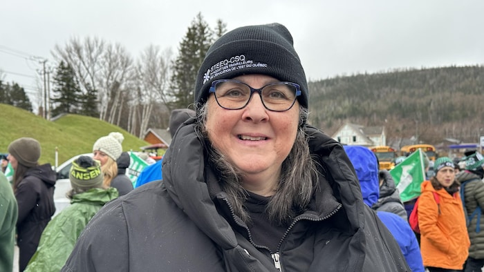 Anne Bernier avec une tuque à l'effigie de son syndicat se tient devant un rassemblement de travailleurs.