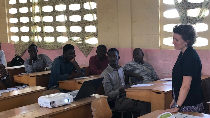Une femme à l'avant d'une classe avec des personnes assises.