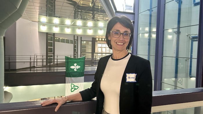 Annie Demers, souriante, pose dans un atrium, devant un drapeau franco-ontarien.