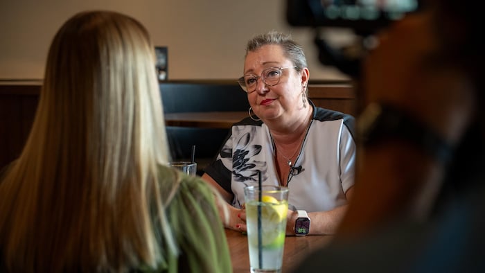 Annie Faucher regarde la journaliste Alexandra Duchaine qui se trouve de dos. Toutes deux sont assises à la table d'un restaurant. Deux limonades se trouvent sur la table.