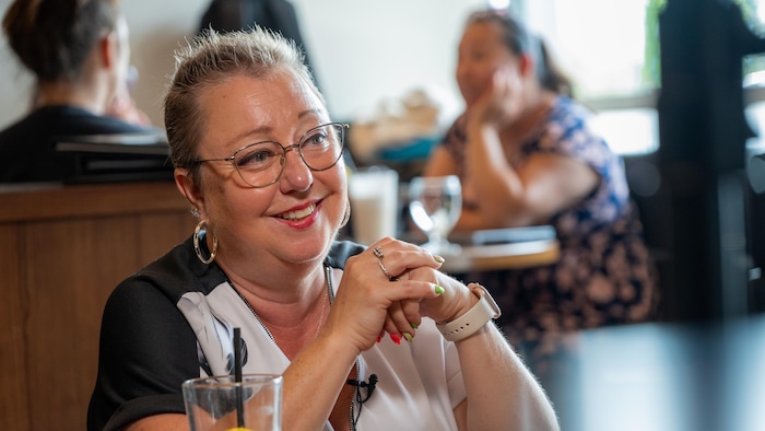 Annie Faucher sourit à la caméra. Elle se trouve dans un restaurant. Des gens se trouvent derrière elle.