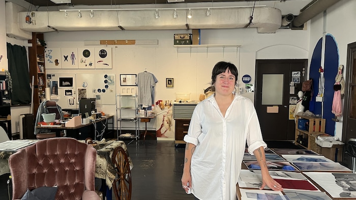 Annie France Noël est debout dans son atelier, au milieu de photographies et de divers objets.