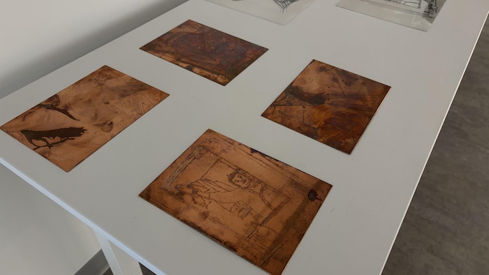 Photo en plongée montrant quatre plaques de métal rectangulaires posées sur une table dans un coin de galerie.