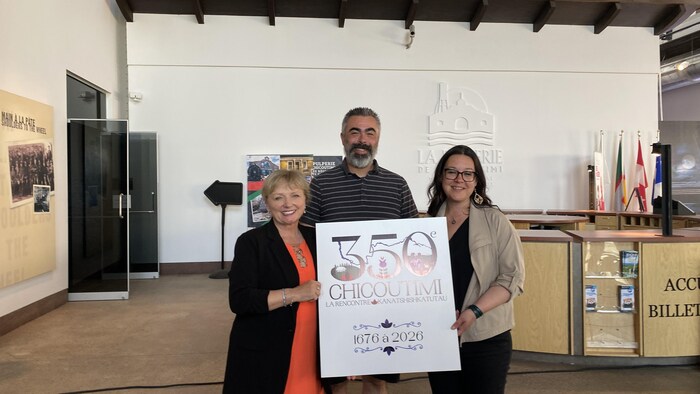 Joan Simard, Patrick Courtois et Julie Dufour tiennent une pancarte du 350e anniversaire de Chicoutimi.