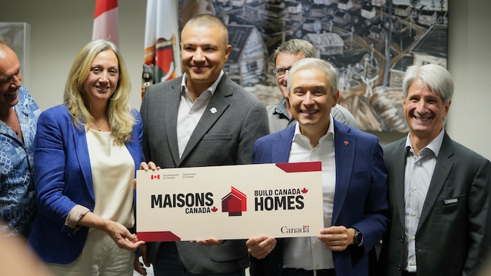 Une femme et trois hommes qui tiennent une pancarte sur laquelle il est écrit Maisons Canada du gouvernement fédéral.