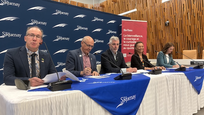 Cinq personnes sont assises à une table avec des micros.