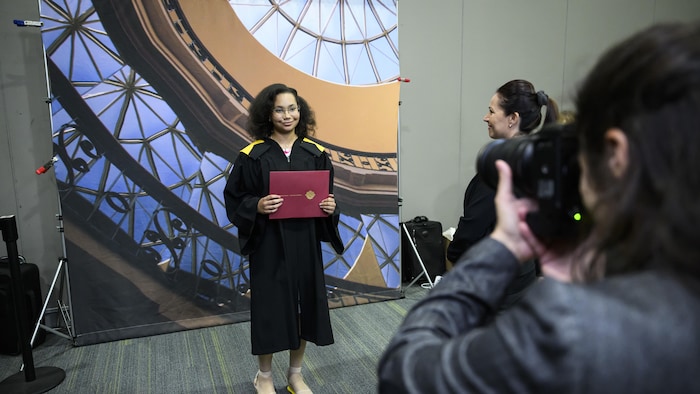 Anthaea-Grace Patricia Dennis, vêtue d'une toge, pose pour la caméra avec son diplôme de l'Université d'Ottawa entre ses mains.