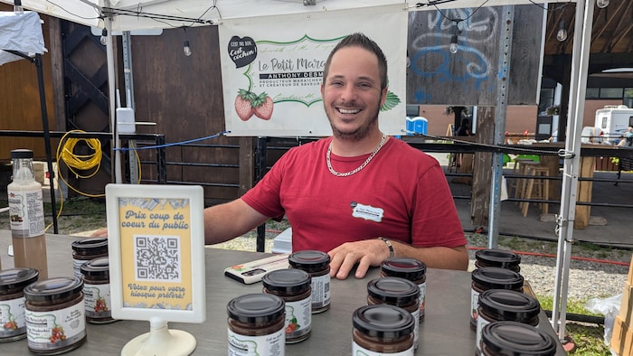 Anthony Desmarais pose à son kiosque, tout sourire, derrière ses produits. 