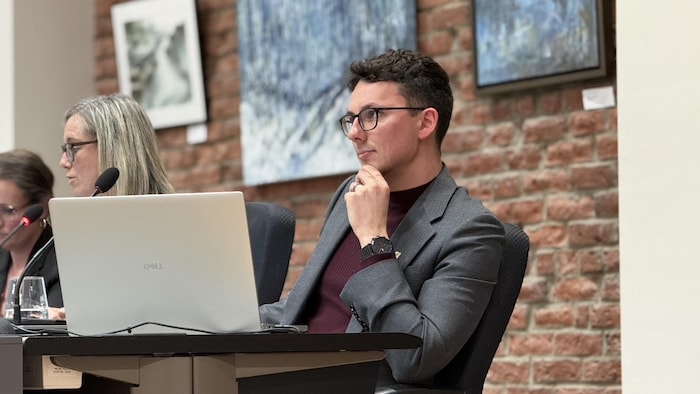 Anthony Dufour derrière un micro et un ordinateur dans la salle du conseil municipal de Lévis.
