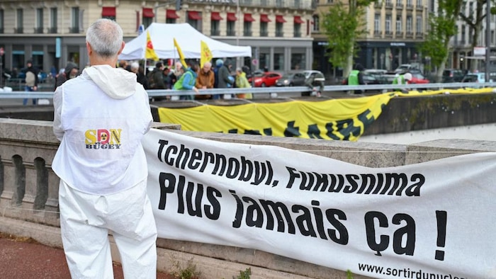 Un militant antinucléaire se tient debout devant une banderole qui porte la mention « Tchernobyl, Fukushima, plus jamais ».