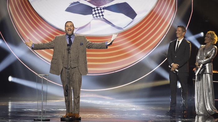 L'acteur ouvre les bras grands en prononçant un discours sur scène.