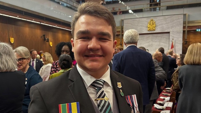 Un jeune homme sourit à la caméra, portant des médailles.