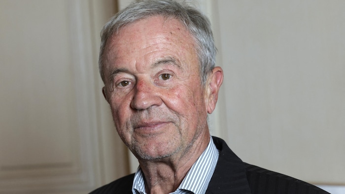 Un homme aux cheveux gris sourit.